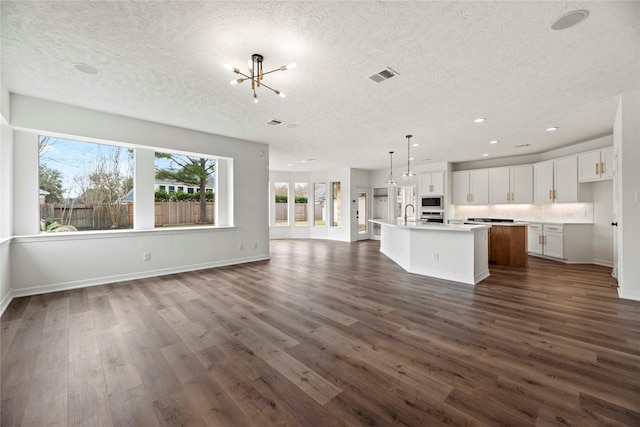 unfurnished living room with a notable chandelier, dark wood-type flooring, sink, and a textured ceiling