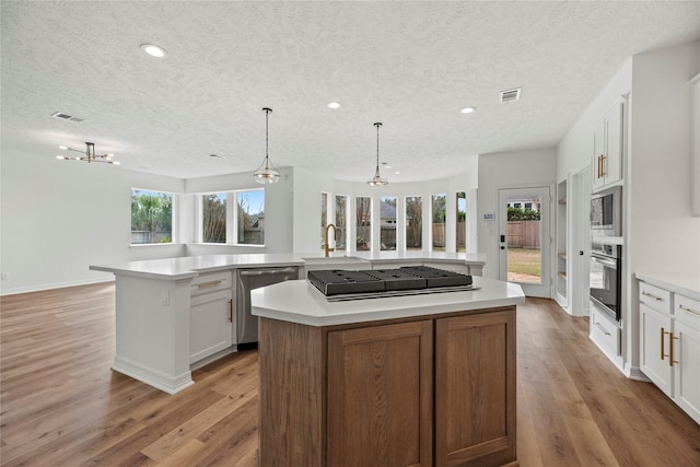 kitchen featuring a kitchen island, appliances with stainless steel finishes, pendant lighting, white cabinetry, and light hardwood / wood-style flooring