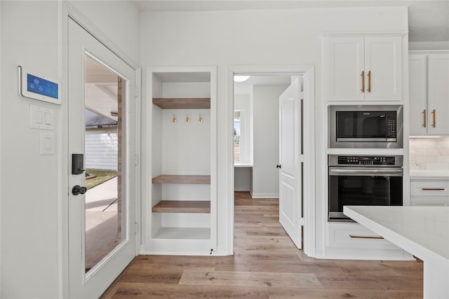 kitchen with light hardwood / wood-style flooring, white cabinets, built in microwave, decorative backsplash, and stainless steel oven