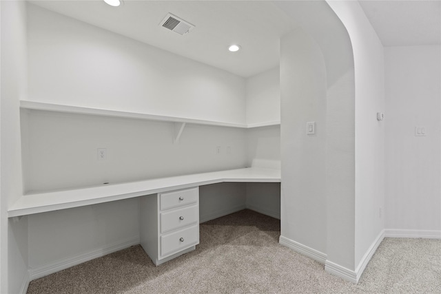 unfurnished office featuring built in desk and light colored carpet