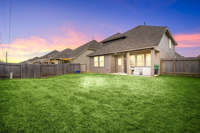 back house at dusk featuring a patio area and a lawn