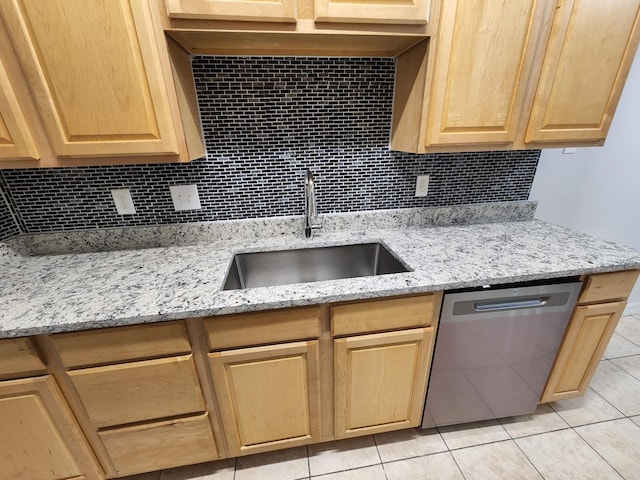 kitchen with stainless steel dishwasher, light brown cabinetry, sink, and light stone countertops