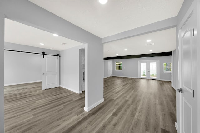 unfurnished living room featuring french doors, a barn door, beam ceiling, and light hardwood / wood-style flooring