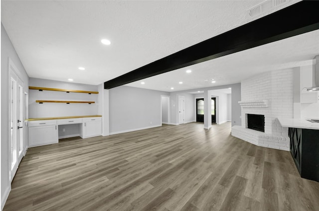 unfurnished living room with a fireplace, beam ceiling, built in desk, and light hardwood / wood-style floors