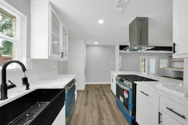 kitchen with sink, appliances with stainless steel finishes, island exhaust hood, light stone countertops, and white cabinets