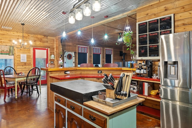 kitchen with finished concrete flooring, wooden walls, pendant lighting, and stainless steel fridge with ice dispenser