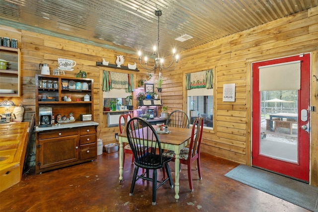 dining room with finished concrete floors, a chandelier, and wood walls