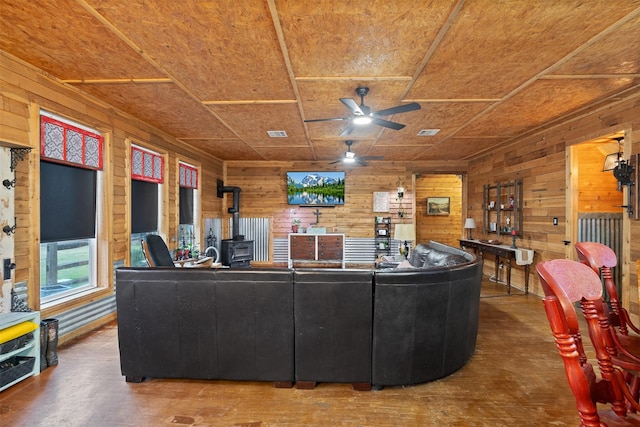 living area with a wood stove, wooden walls, visible vents, and a ceiling fan