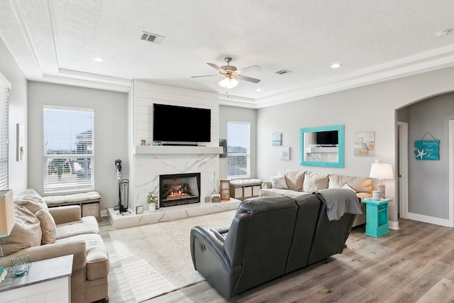 living room with ceiling fan, a high end fireplace, a textured ceiling, and light hardwood / wood-style floors