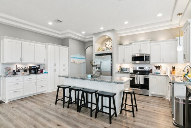 kitchen with a breakfast bar area, white cabinetry, stainless steel appliances, a center island, and light stone counters