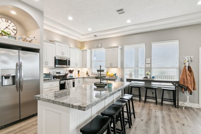 kitchen with a kitchen island, appliances with stainless steel finishes, white cabinets, a kitchen bar, and light stone countertops