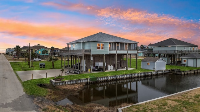 back house at dusk featuring a water view, a storage shed, and a patio