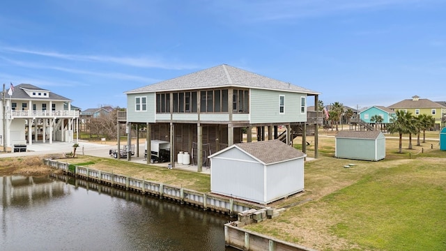 rear view of property featuring a water view, a storage unit, and a yard