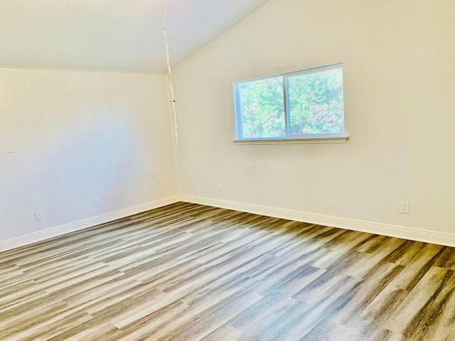 spare room with hardwood / wood-style flooring and vaulted ceiling