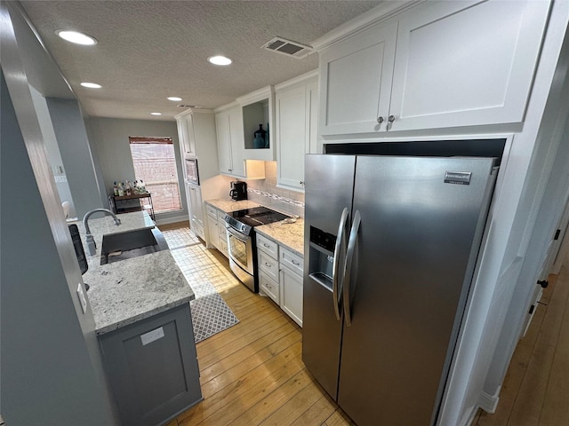 kitchen with sink, white cabinetry, light stone counters, light hardwood / wood-style flooring, and appliances with stainless steel finishes