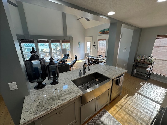 kitchen with lofted ceiling, sink, light stone counters, and light hardwood / wood-style floors