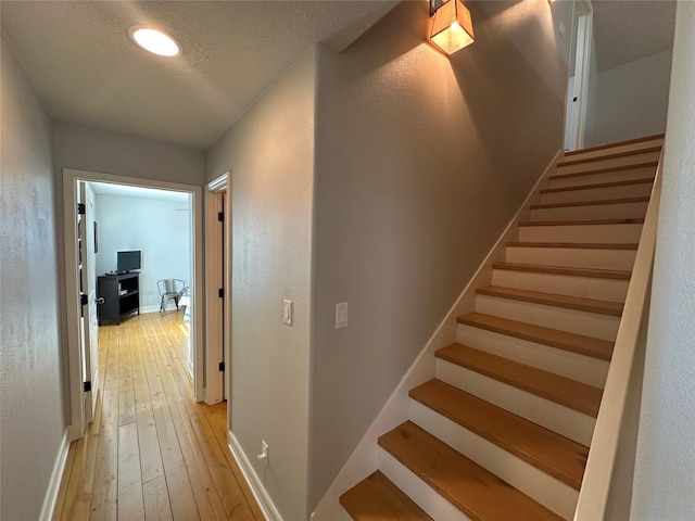 corridor with a textured ceiling and light hardwood / wood-style flooring