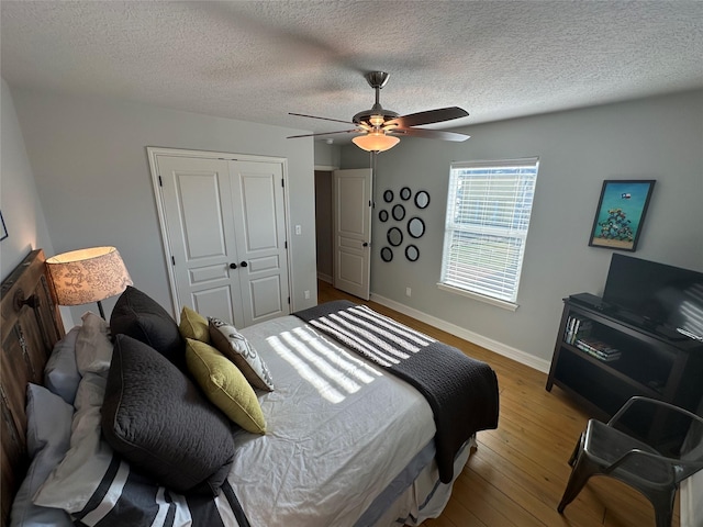 bedroom with ceiling fan, hardwood / wood-style floors, a textured ceiling, and a closet