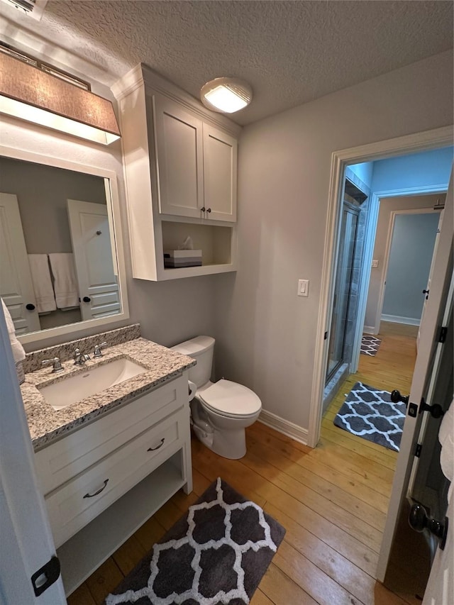 bathroom with vanity, wood-type flooring, a textured ceiling, toilet, and walk in shower