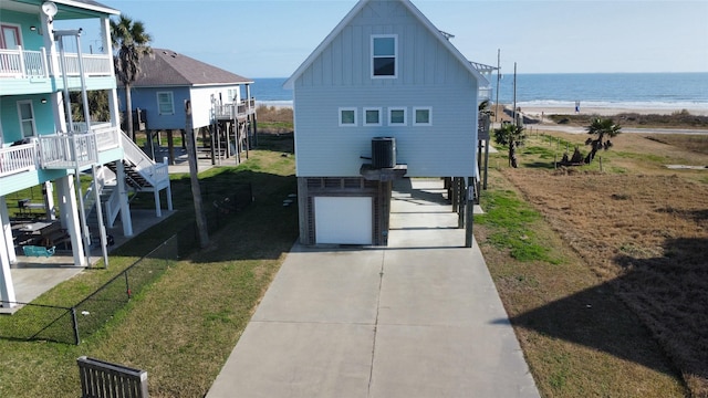 exterior space with cooling unit, a front yard, a water view, a beach view, and a garage