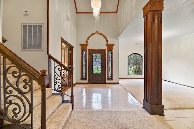 carpeted entrance foyer with decorative columns, crown molding, a high ceiling, and an inviting chandelier