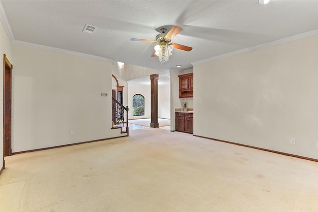 unfurnished living room with decorative columns, ornamental molding, ceiling fan, light carpet, and a textured ceiling