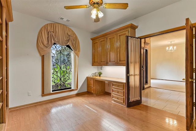 unfurnished office featuring ceiling fan with notable chandelier, built in desk, and light hardwood / wood-style floors