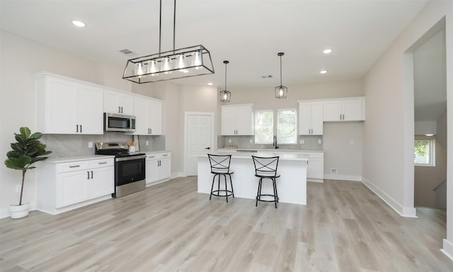 kitchen with pendant lighting, a breakfast bar area, white cabinetry, stainless steel appliances, and a center island