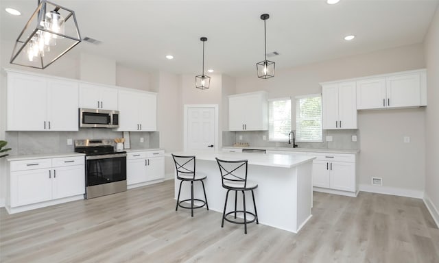 kitchen with stainless steel appliances, a kitchen island, pendant lighting, and white cabinets