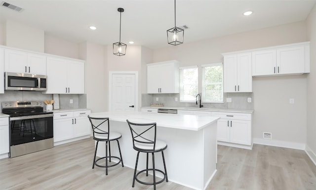 kitchen featuring white cabinetry, appliances with stainless steel finishes, hanging light fixtures, and a kitchen island