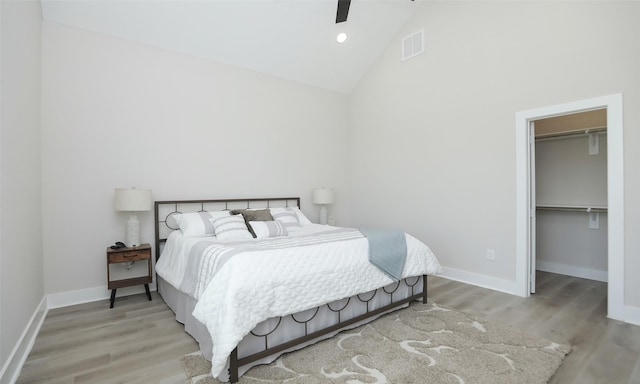 bedroom featuring high vaulted ceiling, a walk in closet, ceiling fan, light hardwood / wood-style floors, and a closet