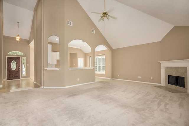 unfurnished living room featuring a tiled fireplace, high vaulted ceiling, light carpet, and ceiling fan