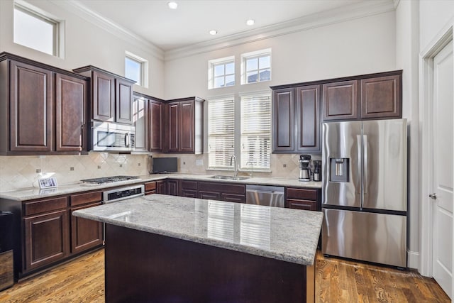 kitchen with sink, crown molding, stainless steel appliances, a center island, and light stone countertops