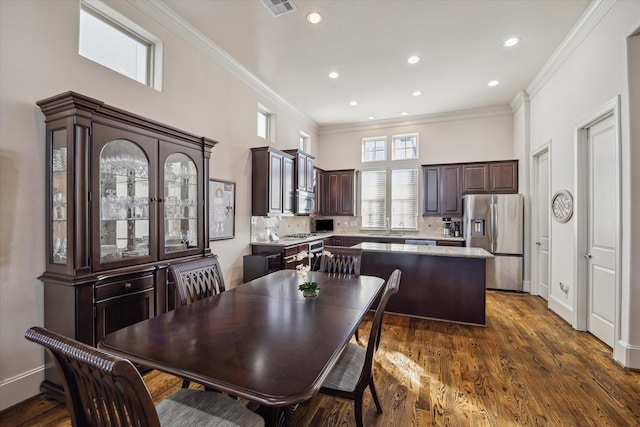 dining space with dark wood-type flooring, a towering ceiling, and crown molding