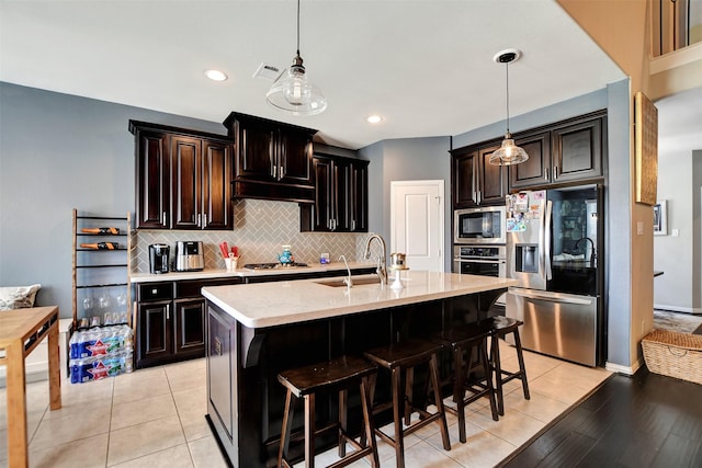 kitchen with sink, appliances with stainless steel finishes, dark brown cabinets, an island with sink, and decorative light fixtures