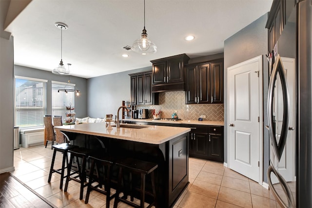 kitchen with pendant lighting, sink, a center island with sink, and stainless steel refrigerator