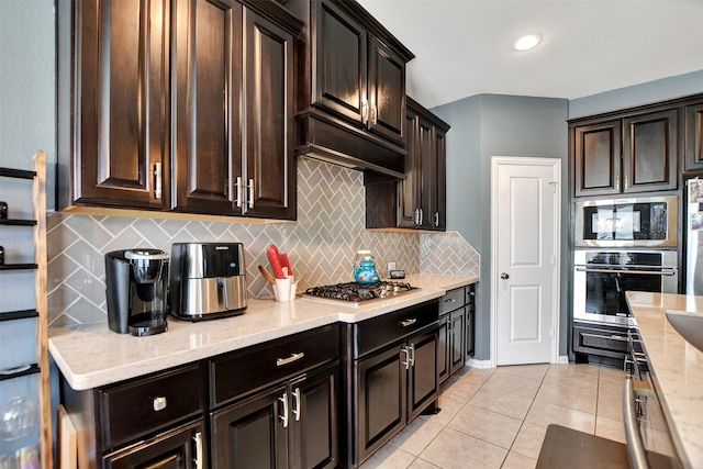 kitchen with light tile patterned floors, backsplash, dark brown cabinets, stainless steel appliances, and light stone counters