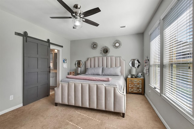 bedroom featuring ceiling fan, light colored carpet, ensuite bathroom, and a barn door