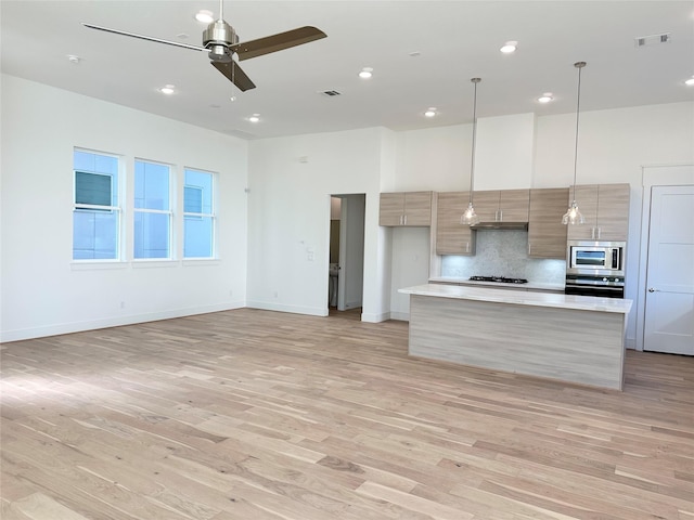 kitchen featuring light hardwood / wood-style flooring, ceiling fan, appliances with stainless steel finishes, hanging light fixtures, and tasteful backsplash