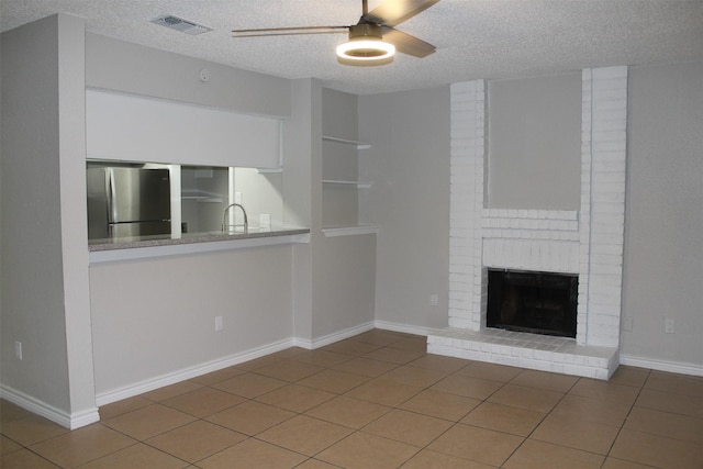 unfurnished living room with tile patterned floors, sink, a textured ceiling, ceiling fan, and a fireplace