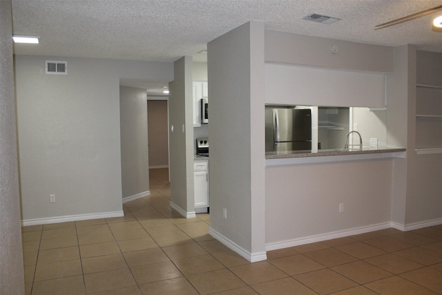 kitchen featuring white cabinets, stainless steel appliances, a textured ceiling, and light tile patterned floors