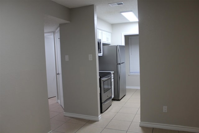 kitchen featuring a textured ceiling, light tile patterned flooring, white cabinets, and appliances with stainless steel finishes