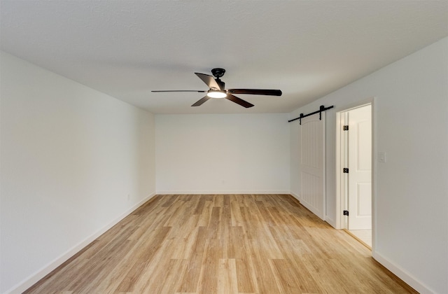 spare room with ceiling fan, a barn door, a textured ceiling, and light wood-type flooring