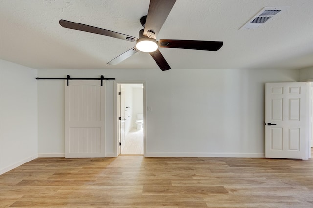 unfurnished room featuring light hardwood / wood-style flooring, a barn door, and a textured ceiling