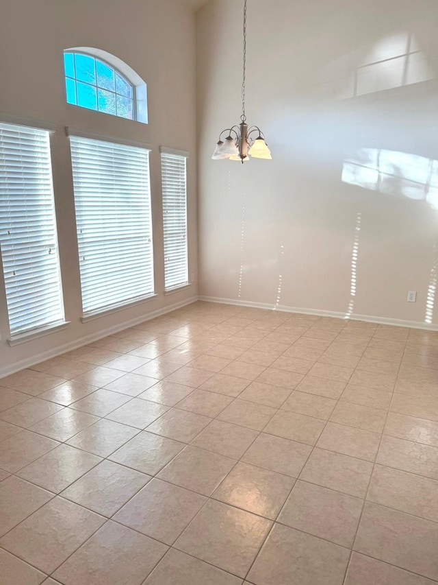 tiled empty room featuring a high ceiling and an inviting chandelier