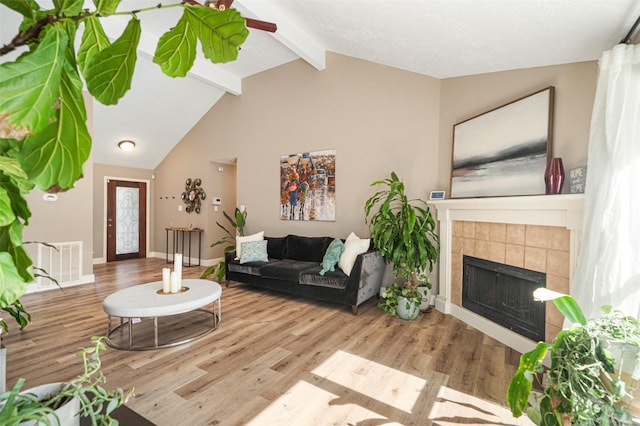 living room with a tiled fireplace, lofted ceiling with beams, and light hardwood / wood-style floors