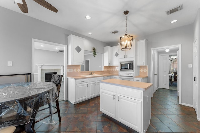 kitchen with a kitchen island, stainless steel microwave, white cabinetry, oven, and hanging light fixtures