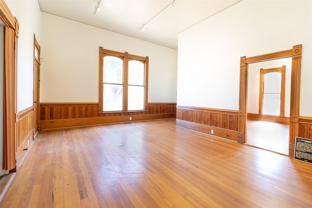 spare room featuring track lighting, wooden walls, and light wood-type flooring