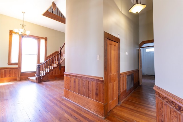 entrance foyer featuring a high ceiling, wooden walls, an inviting chandelier, and dark hardwood / wood-style flooring