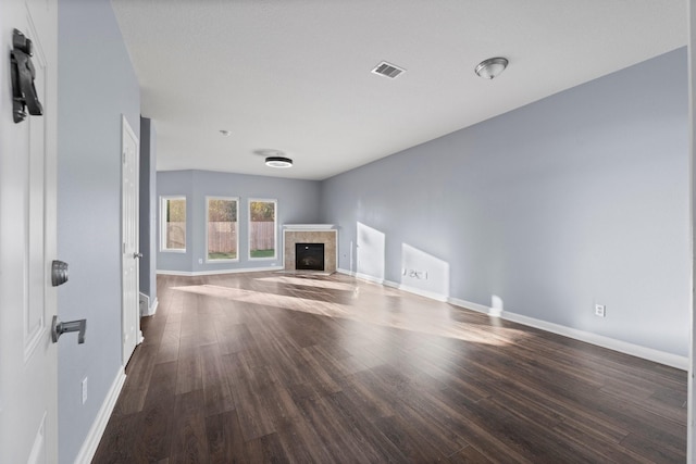 unfurnished living room featuring a tiled fireplace and dark wood-type flooring